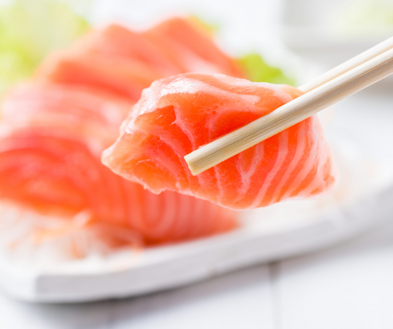 closed up of salmon sashimi set with chopsticks holding a piece of sliced salmon, healthy food and diet